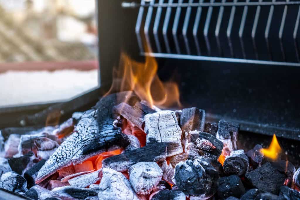 Een close-up van een barbecue met vlammende houtskool en houtskool, die de hitte en textuur van de gestookte kolen benadrukt, perfect om te grillen.