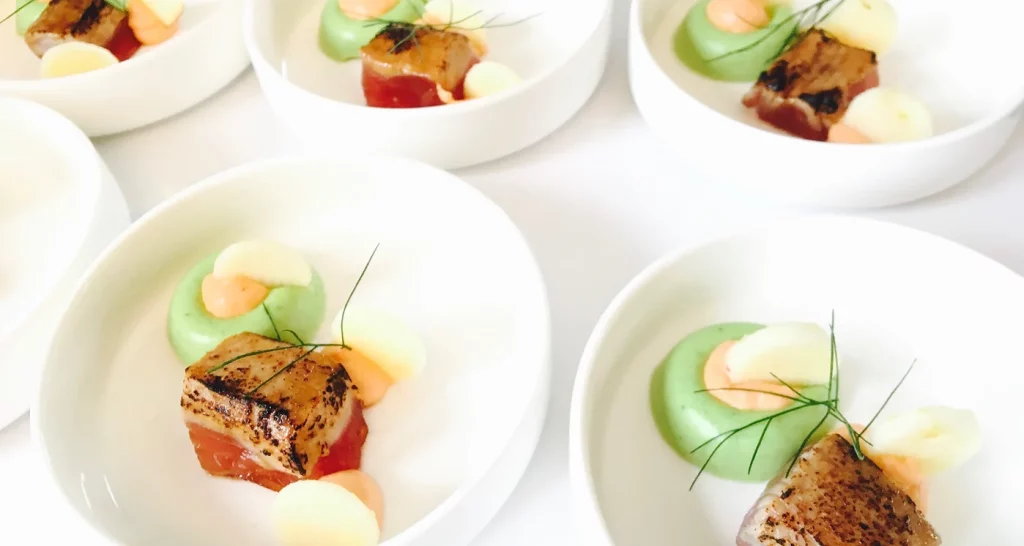 Elegante gastronomische hapjes voor privéfeesten: geschroeide Sint-Jakobsschelpen met kleurrijke puree en garnituren, kunstig gepresenteerd in witte kommen.